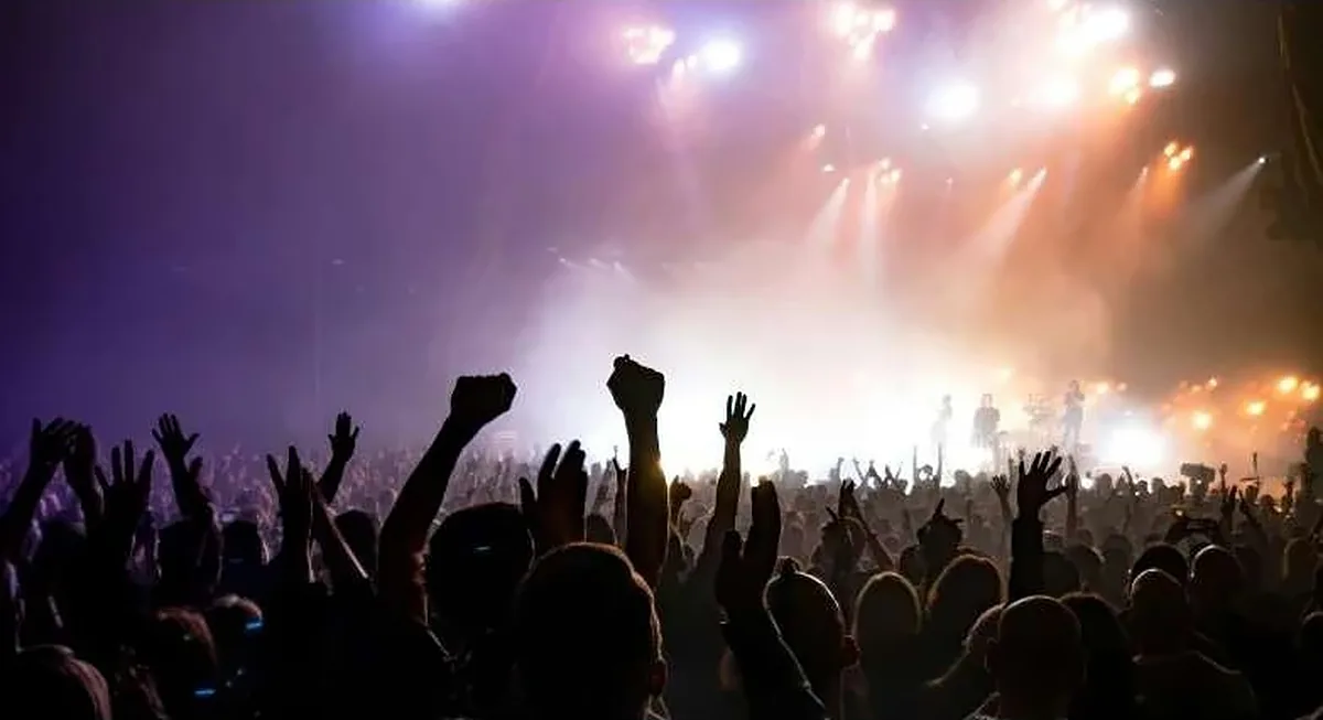 Concert audience raising their hands beneath colourful stage lights