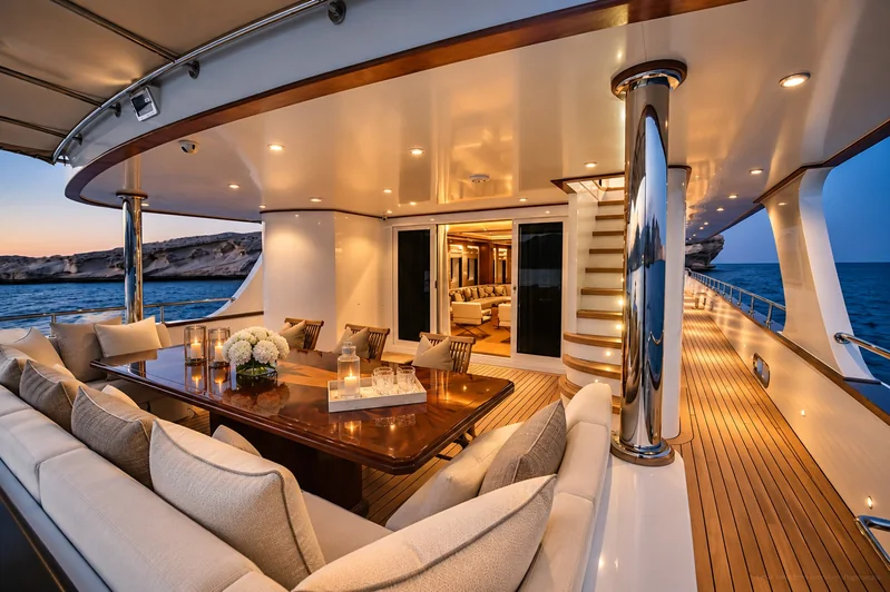 Covered aft deck aboard AMARA with a dining table and lounge seating at dusk