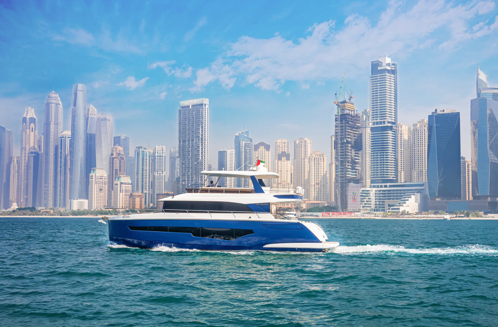 Marinova Classic C62 Blue under way, its blue hull side on to the camera with the Dubai Marina skyline behind.