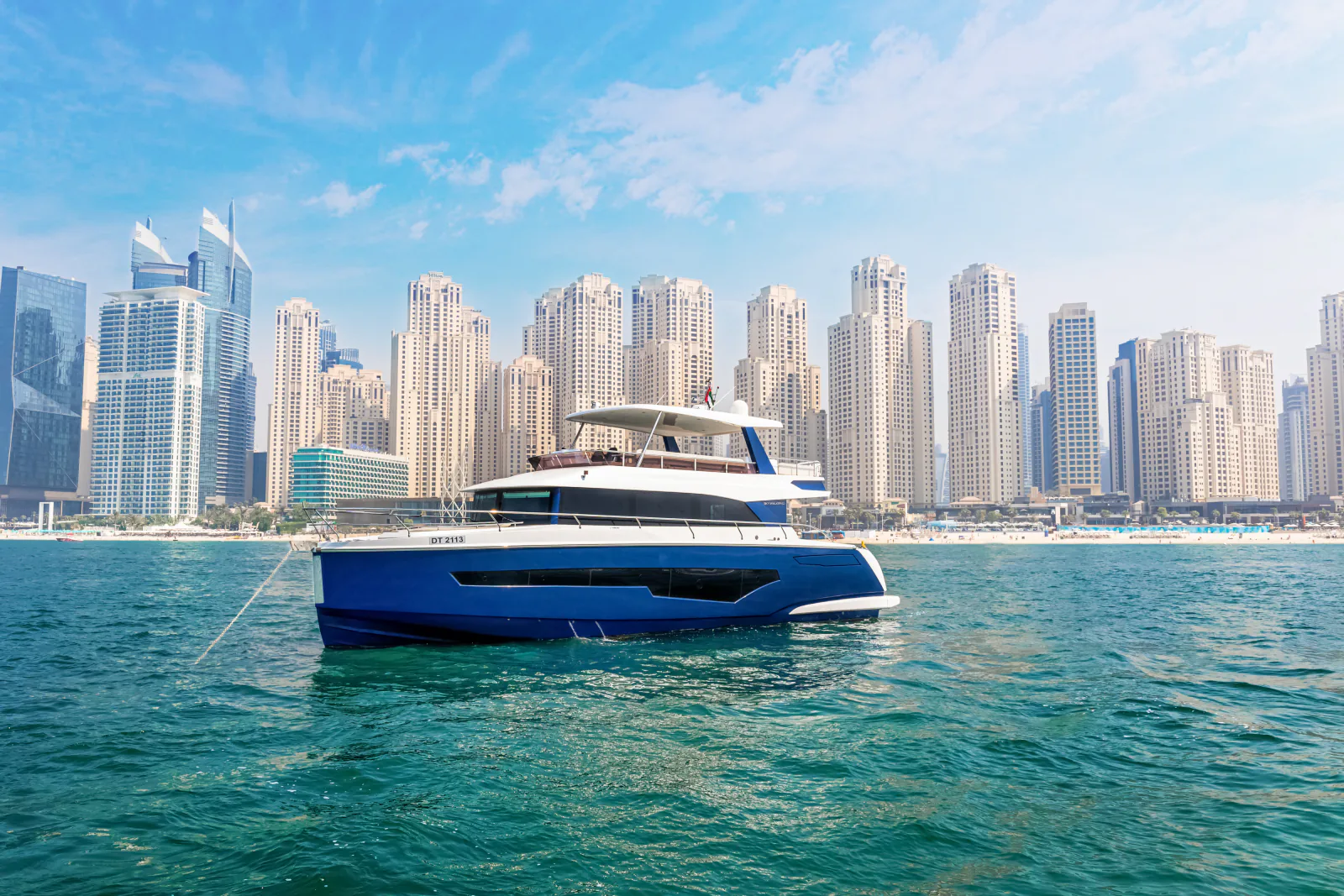 62 feet yacht rental Dubai: the blue hull yacht at rest in full side profile against a line of waterfront towers.