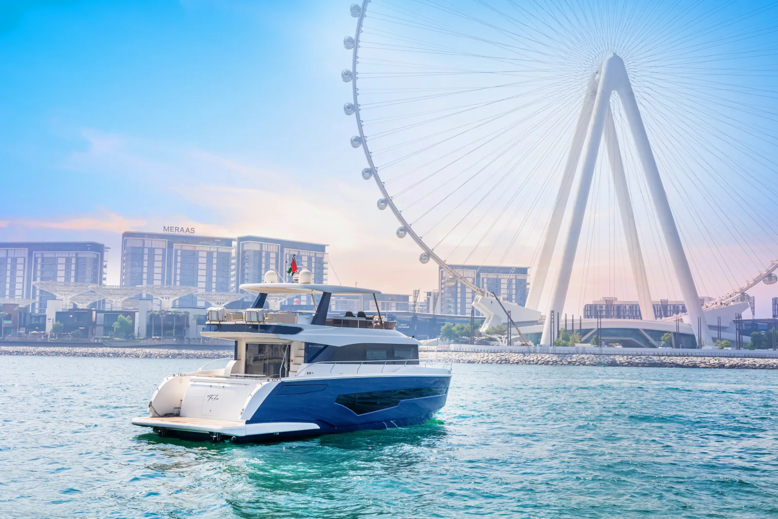 62 feet yacht rental Dubai: a stern quarter view of the blue yacht with a large observation wheel behind it.