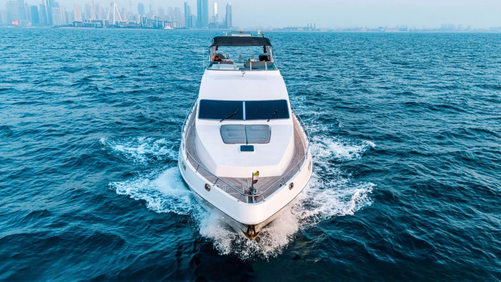 Majesty 77 yacht head on with the bow toward the camera and a city skyline behind.