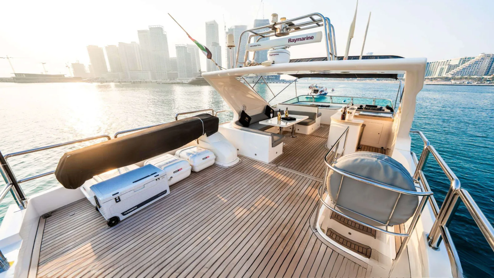 Majesty 77 yacht flybridge deck with a cushioned lounger, a radar arch above and a city skyline beyond.